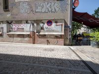 a street with lots of graffiti written on the side of it near a building and people walking