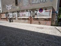 a street with lots of graffiti written on the side of it near a building and people walking