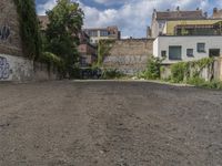 the black writing on the wall is graffiti covered with trees and rocks with houses in the background