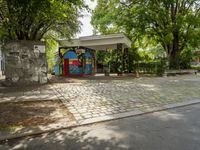 a mural on a stone wall at a bus stop with graffiti covering it in front of trees