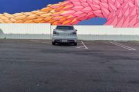 a car parked in front of a painted mural of a feather on the side of a building