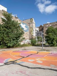 the colorful painted basketball court is on the sidewalk in front of tall buildings with trees