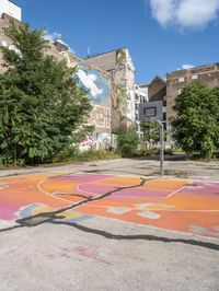 the colorful painted basketball court is on the sidewalk in front of tall buildings with trees