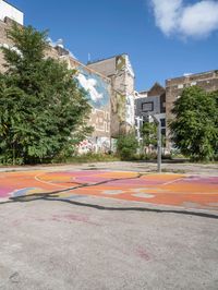 the colorful painted basketball court is on the sidewalk in front of tall buildings with trees