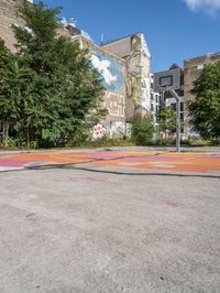 the colorful painted basketball court is on the sidewalk in front of tall buildings with trees