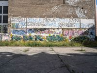 graffiti covers a wall of vacant land with a fire hydrant and green grass near by