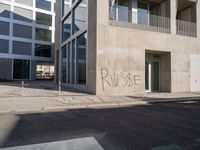 the graffiti is spray painted on the wall near a parking lot of buildings across from it