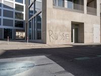 the graffiti is spray painted on the wall near a parking lot of buildings across from it