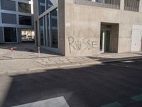 the graffiti is spray painted on the wall near a parking lot of buildings across from it