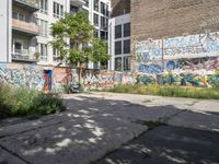 a graffiti wall next to an empty urban street with no traffic signs on it and trees in the background