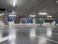 an empty parking lot with graffiti painted on the walls in different languages and colors with a single white arrow pointing down at it