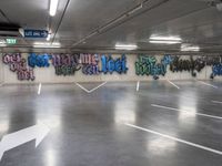 an empty parking lot with graffiti painted on the walls in different languages and colors with a single white arrow pointing down at it