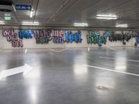 an empty parking lot with graffiti painted on the walls in different languages and colors with a single white arrow pointing down at it