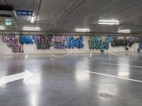 an empty parking lot with graffiti painted on the walls in different languages and colors with a single white arrow pointing down at it