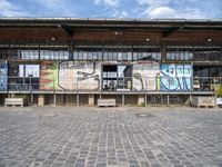 a building has grafitti on the side and an open floor in it and a parking area with benches