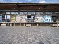 a building has grafitti on the side and an open floor in it and a parking area with benches