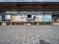 a building has grafitti on the side and an open floor in it and a parking area with benches