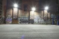 a wall covered in graffiti sitting on the side of a road under streetlights at night