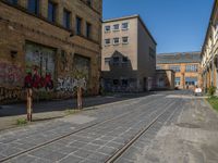 empty street in urban area with tracks on both sides of it, brick buildings, graffiti, green trees and street signs on both sides