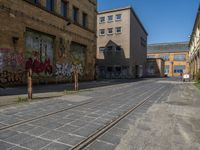 empty street in urban area with tracks on both sides of it, brick buildings, graffiti, green trees and street signs on both sides