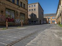 empty street in urban area with tracks on both sides of it, brick buildings, graffiti, green trees and street signs on both sides