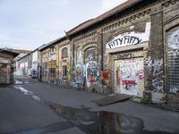 graffiti in a street with wet pavement and buildings with signs on them and a puddle