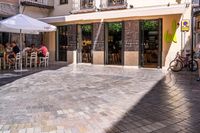 people walk in the empty streets near small tables and umbrellas and a building with balconies on the windows