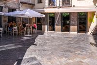 people walk in the empty streets near small tables and umbrellas and a building with balconies on the windows