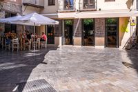 people walk in the empty streets near small tables and umbrellas and a building with balconies on the windows