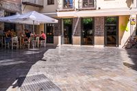 people walk in the empty streets near small tables and umbrellas and a building with balconies on the windows