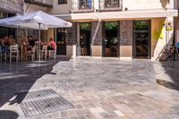 people walk in the empty streets near small tables and umbrellas and a building with balconies on the windows