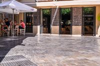 people walk in the empty streets near small tables and umbrellas and a building with balconies on the windows