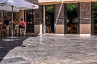 people walk in the empty streets near small tables and umbrellas and a building with balconies on the windows