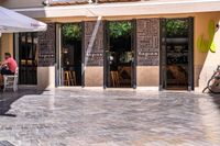 people walk in the empty streets near small tables and umbrellas and a building with balconies on the windows