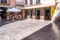 people walk in the empty streets near small tables and umbrellas and a building with balconies on the windows