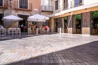 people walk in the empty streets near small tables and umbrellas and a building with balconies on the windows