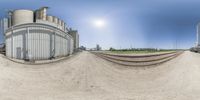 a fisheye view of a train track in an empty industrial area with buildings and other structures