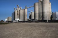 many large steel grain silos line a field with cars in the background on a clear blue sky