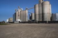 many large steel grain silos line a field with cars in the background on a clear blue sky