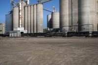 many large steel grain silos line a field with cars in the background on a clear blue sky