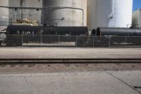 a black train engine parked next to a concrete fence and cement tanks in the background