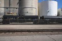 a black train engine parked next to a concrete fence and cement tanks in the background