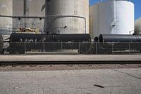 a black train engine parked next to a concrete fence and cement tanks in the background