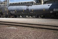 a black train parked next to a group of tanks next to a building and a lot of tracks