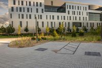 a city street surrounded by grass and tall buildings at the end of a street there is a paved pathway in front of the building