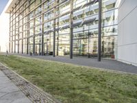 the building has glass walls and a sidewalk with green grass in it outside of it