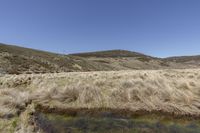 a small stream running through a grass covered hillside near a mountain range in the distance