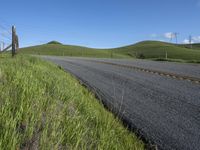 the grass grows in between the roadway and road area of a rural area under a bright blue sky