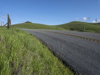 the grass grows in between the roadway and road area of a rural area under a bright blue sky