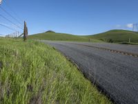 the grass grows in between the roadway and road area of a rural area under a bright blue sky